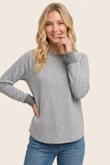 woman wearing a gray long sleeve casual top with contrasting cuff details and smiling at the camera