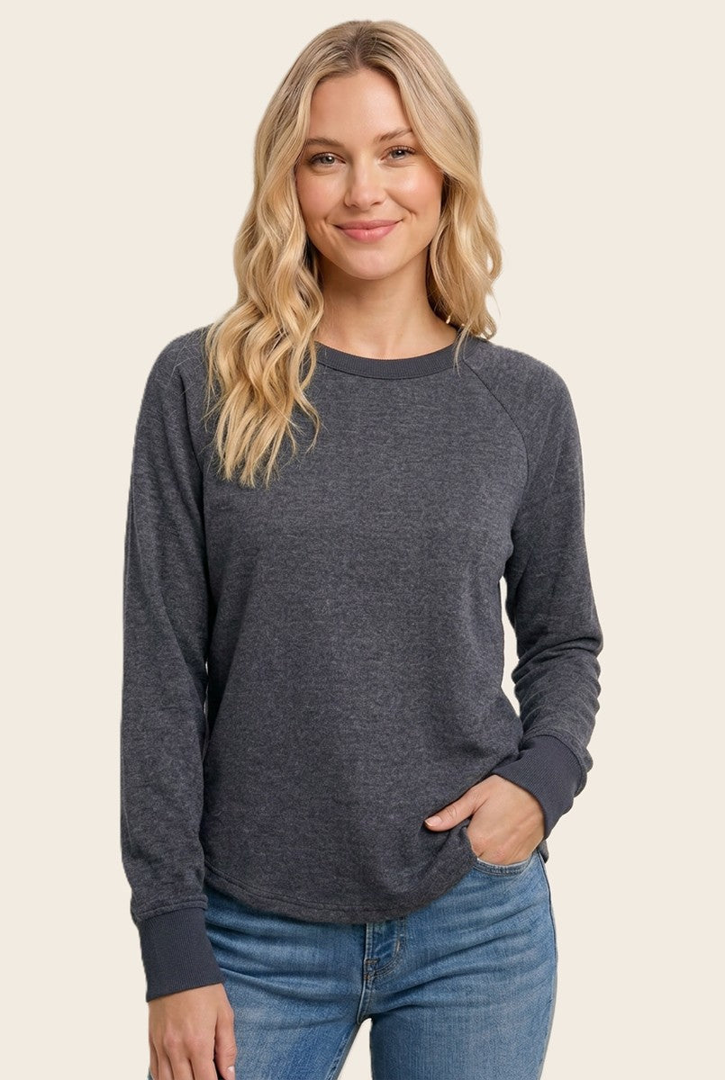 woman wearing a dark gray long sleeve sweatshirt with a rounded hem and gray ribbed cuffs, smiling at the camera
