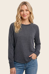 woman wearing a dark gray long sleeve sweatshirt with a rounded hem and gray ribbed cuffs, smiling at the camera