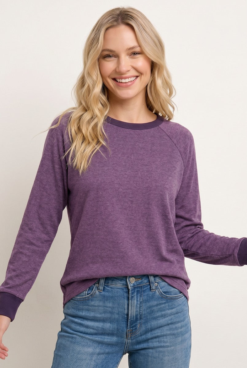 woman wearing a purple long sleeve raglan sweatshirt with contrasting cuffs and relaxed fit, paired with light blue jeans