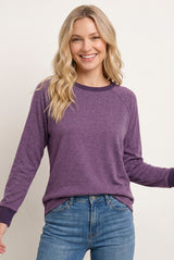 woman wearing a purple long sleeve raglan sweatshirt with contrasting cuffs and relaxed fit, paired with light blue jeans