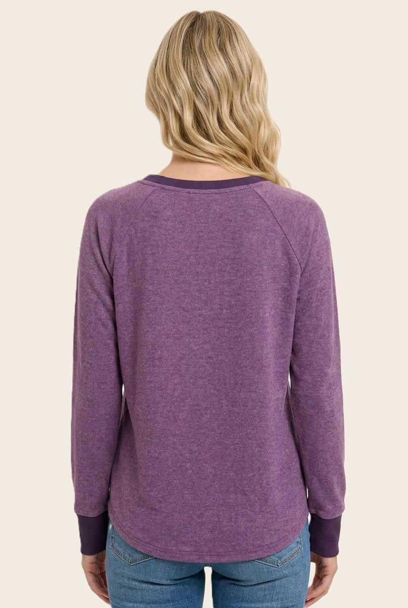 woman wearing a purple long sleeve top with raglan sleeves and a rounded hem, viewed from the back