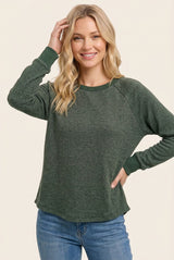 woman wearing a green long sleeve raglan sweatshirt with contrasting cuffs and a relaxed fit while smiling