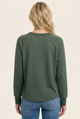 woman wearing a green long sleeve pullover top with raglan sleeves and a casual fit, viewed from the back
