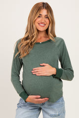 woman wearing a dark green long sleeve maternity top and holding her baby bump