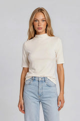 woman wearing a cream short sleeve mock neck top with a fitted style and light blue high-waisted jeans
