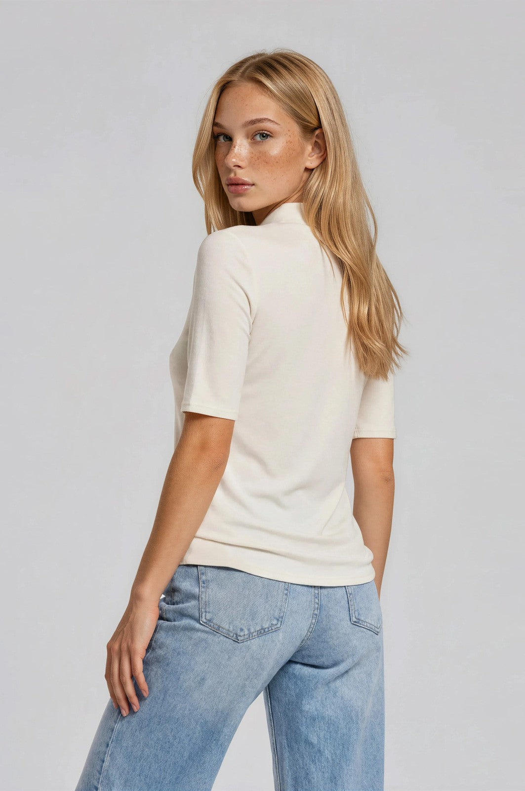 woman wearing a cream short sleeve top and light blue relaxed fit jeans, facing away from the camera