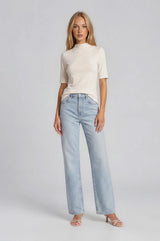 woman wearing a cream short sleeve mock neck top and light blue wide leg jeans with heeled sandals.