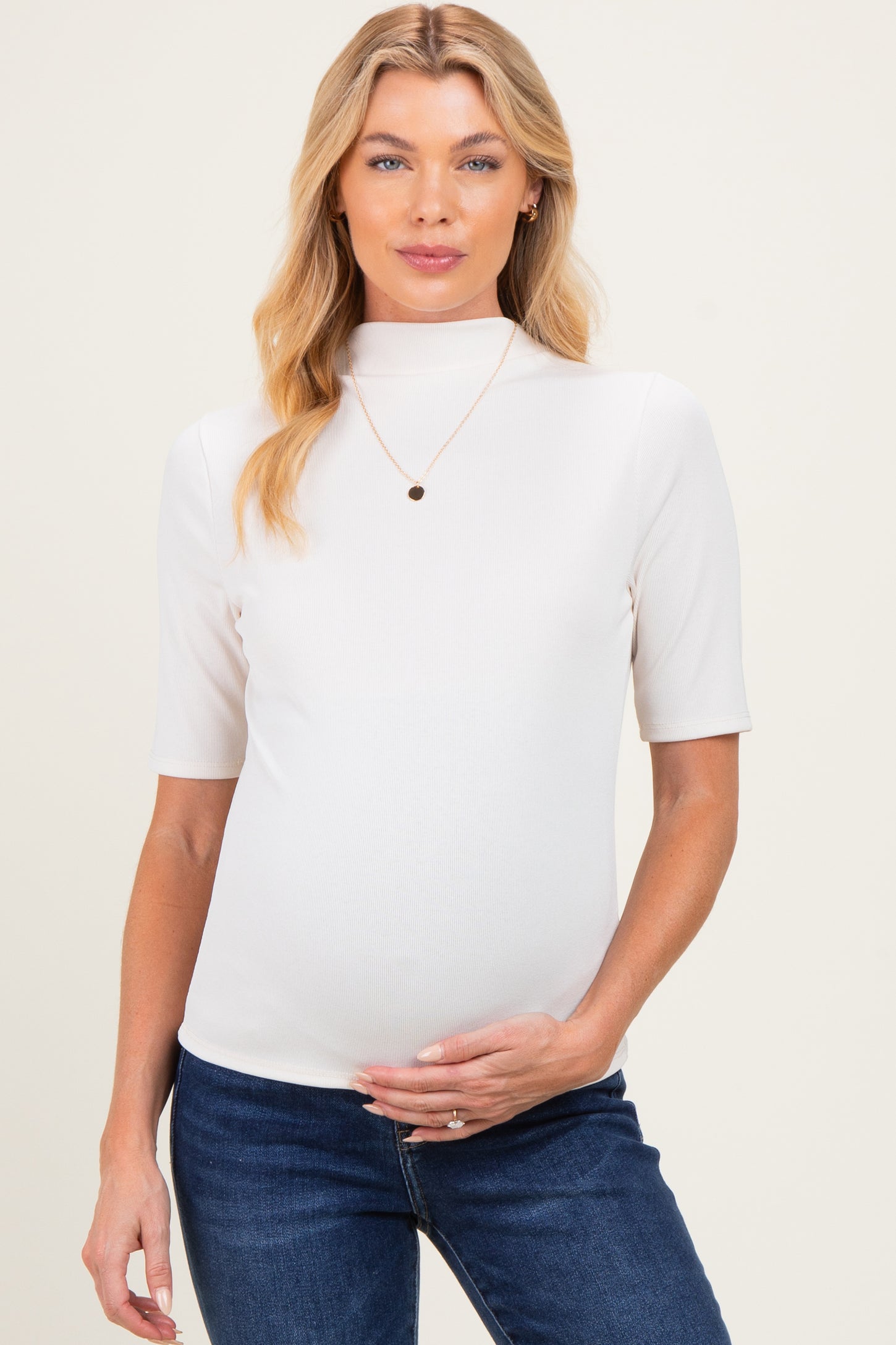 woman wearing a cream short sleeve maternity top, showing a baby bump, paired with denim jeans