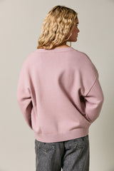woman wearing a pastel pink oversized sweater with a wide neckline and relaxed fit, viewed from the back
