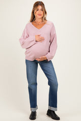 woman wearing a pink v-neck maternity sweater and holding her baby bump, paired with blue jeans and black ankle boots