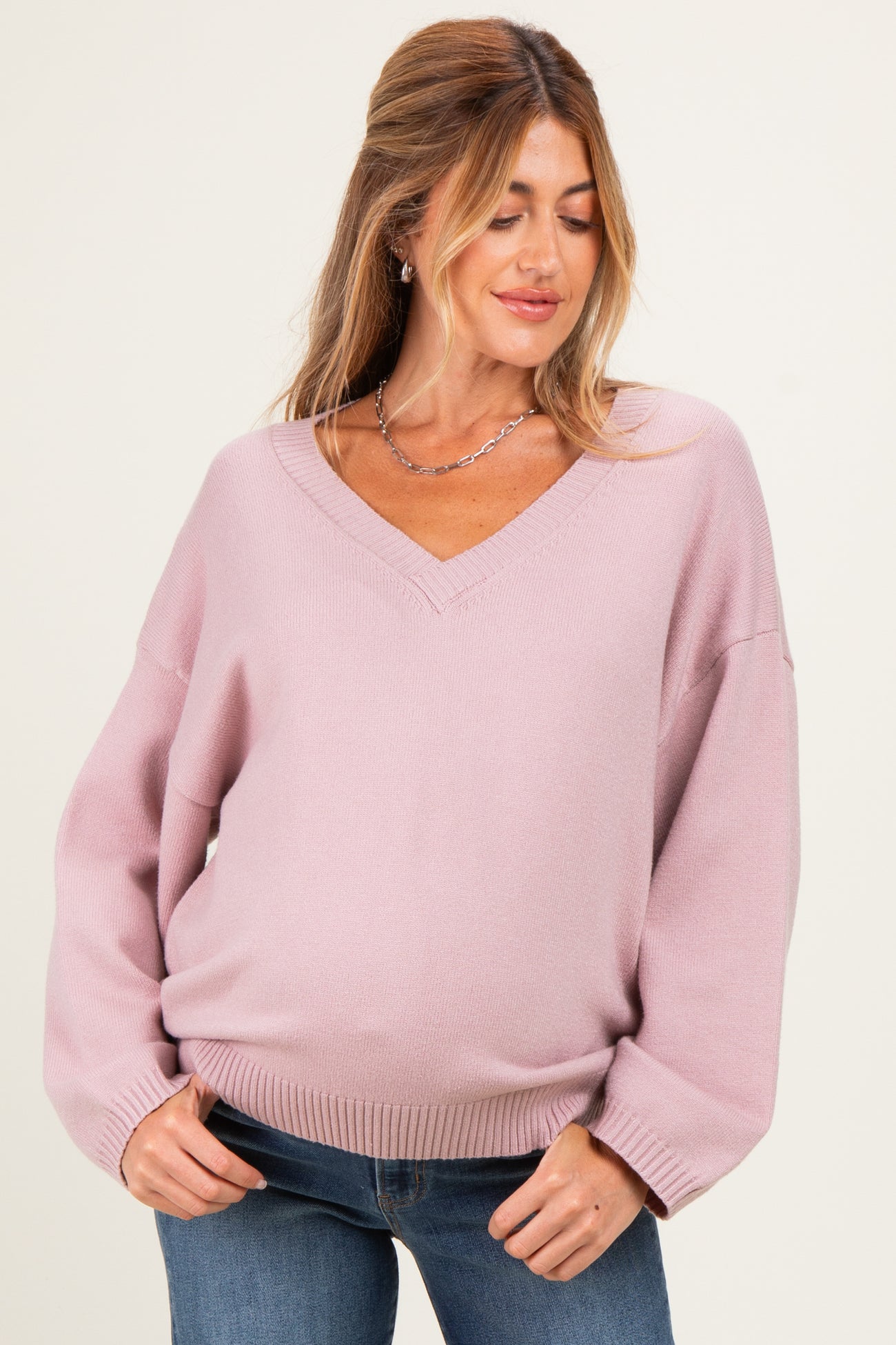 woman wearing a light pink v-neck maternity sweater with bell sleeves and a visible baby bump