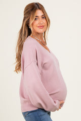 woman wearing a light pink v-neck maternity sweater and showing her baby bump