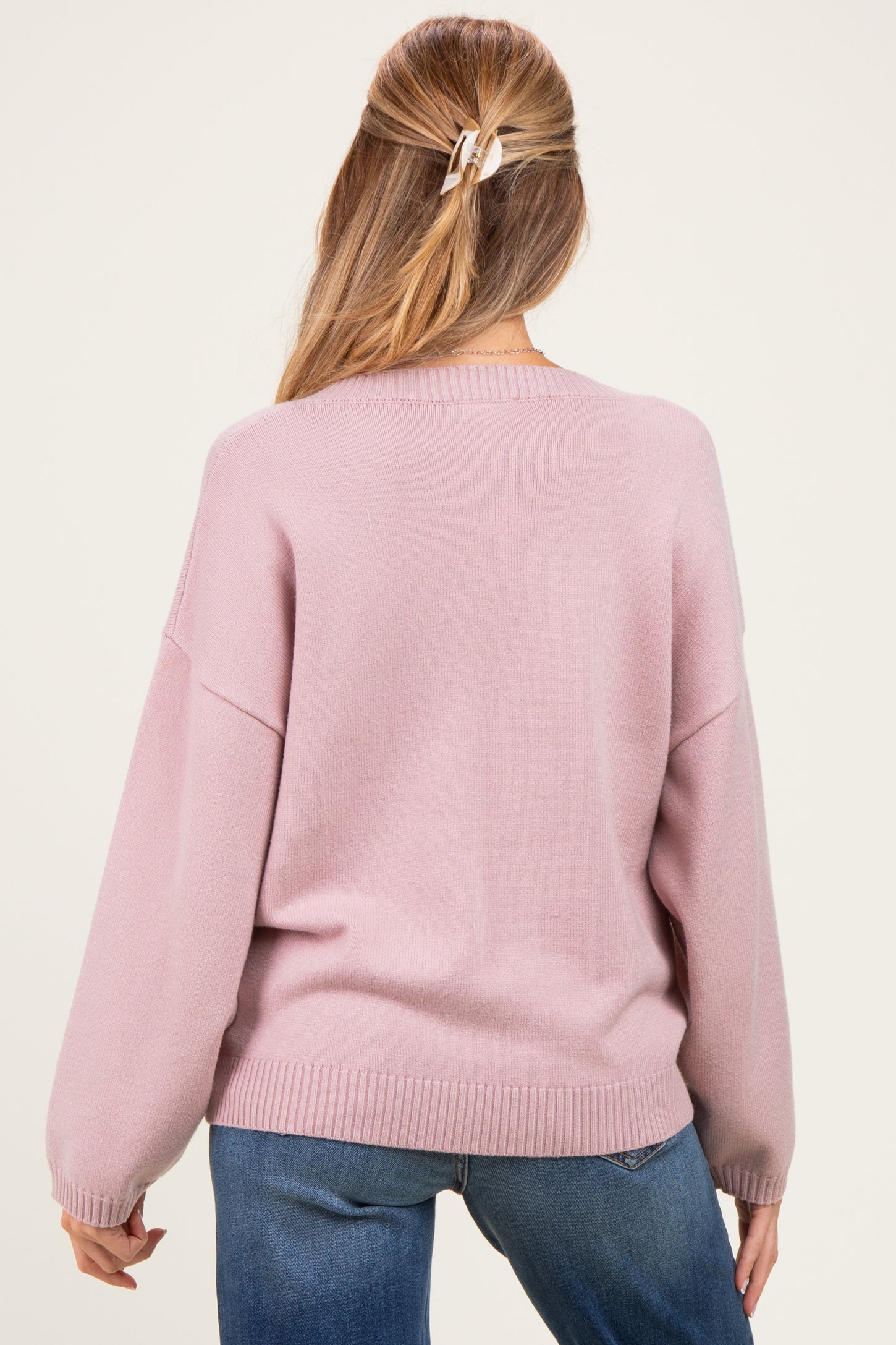 woman wearing a light pink oversized maternity sweater, showing the back view