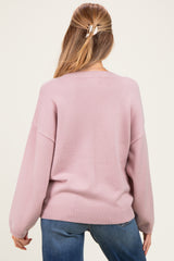 woman wearing a light pink oversized maternity sweater, showing the back view