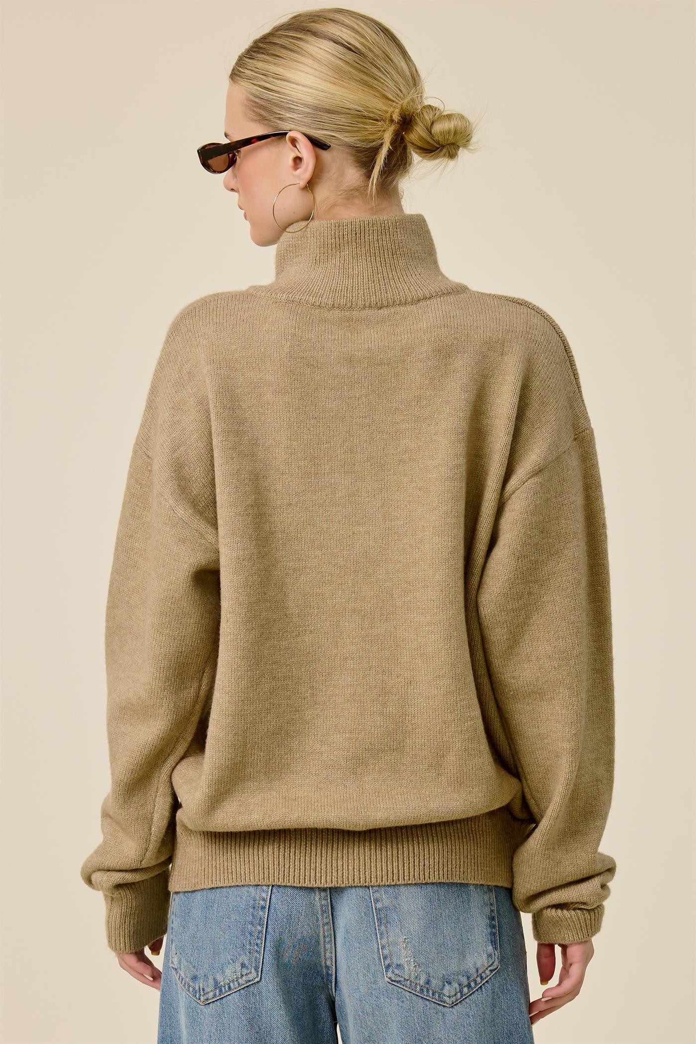 woman wearing an oversized tan turtleneck sweater with rolled sleeves and a relaxed fit, viewed from the back