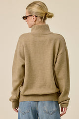 woman wearing an oversized tan turtleneck sweater with rolled sleeves and a relaxed fit, viewed from the back