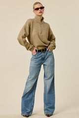 woman wearing a tan zip-up sweater and wide-leg blue jeans, styled with sunglasses and a statement belt