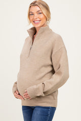 woman wearing a beige zip-up maternity sweater and holding her baby bump