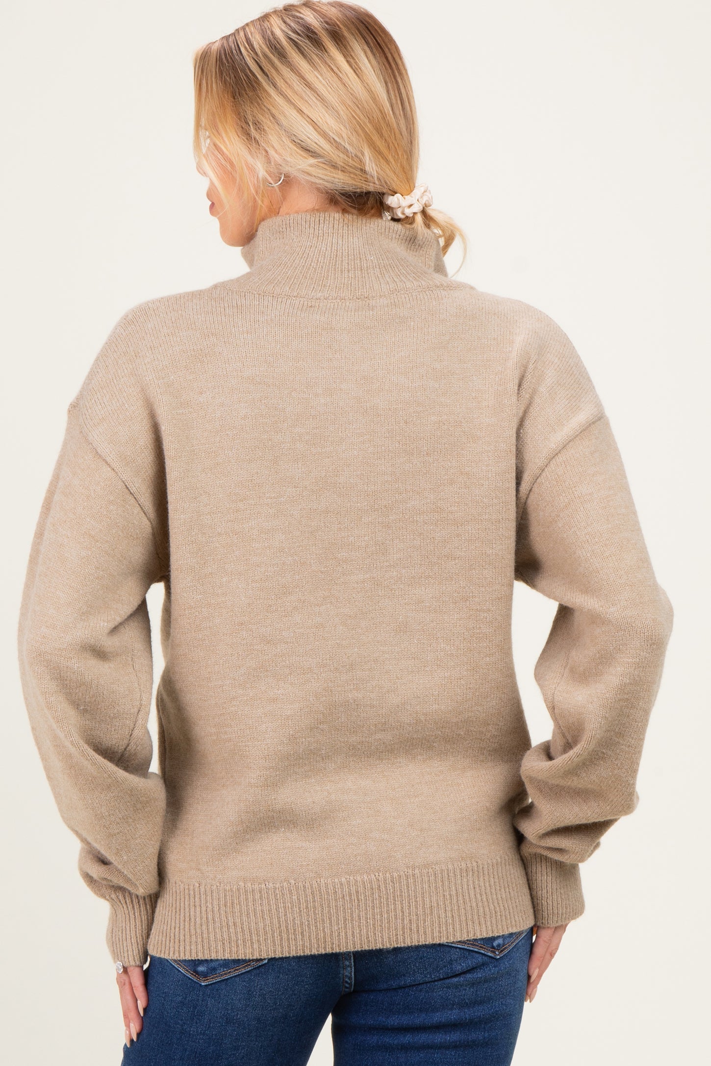 woman wearing a beige oversized maternity sweater with a high collar and long sleeves, showing the back view