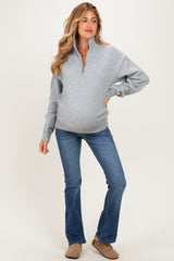woman wearing a gray maternity sweatshirt with half zip and blue flared jeans, showing her baby bump
