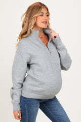 woman wearing a light grey zip-up maternity sweater with a relaxed fit and visible baby bump, paired with blue jeans