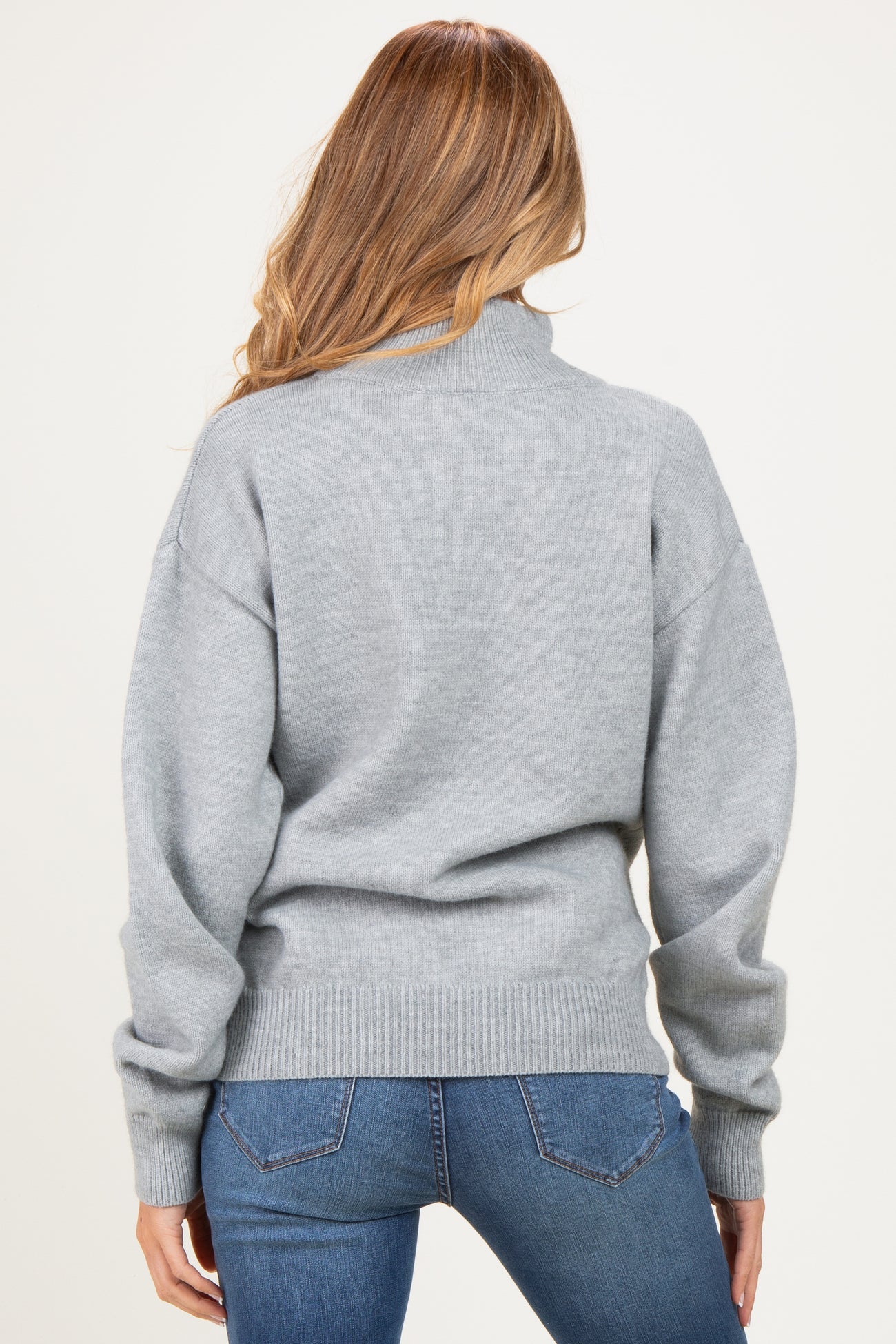 woman wearing a gray maternity sweater with a turtleneck and relaxed fit, seen from the back