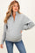 woman wearing a light gray maternity pullover sweater with a half-zip and a visible baby bump