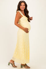 woman wearing a yellow lace maternity dress with ruffled details and holding her baby bump
