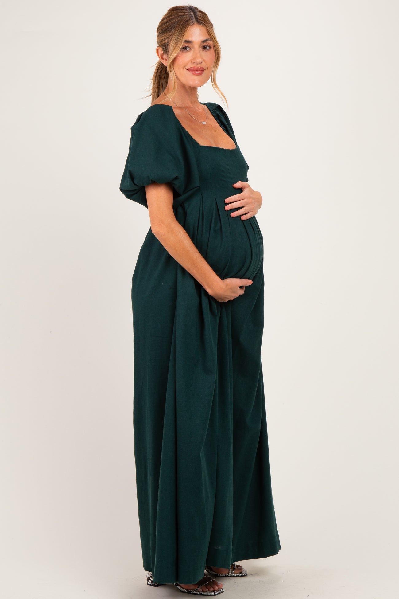 woman wearing a dark green short sleeve maternity dress holding her baby bump