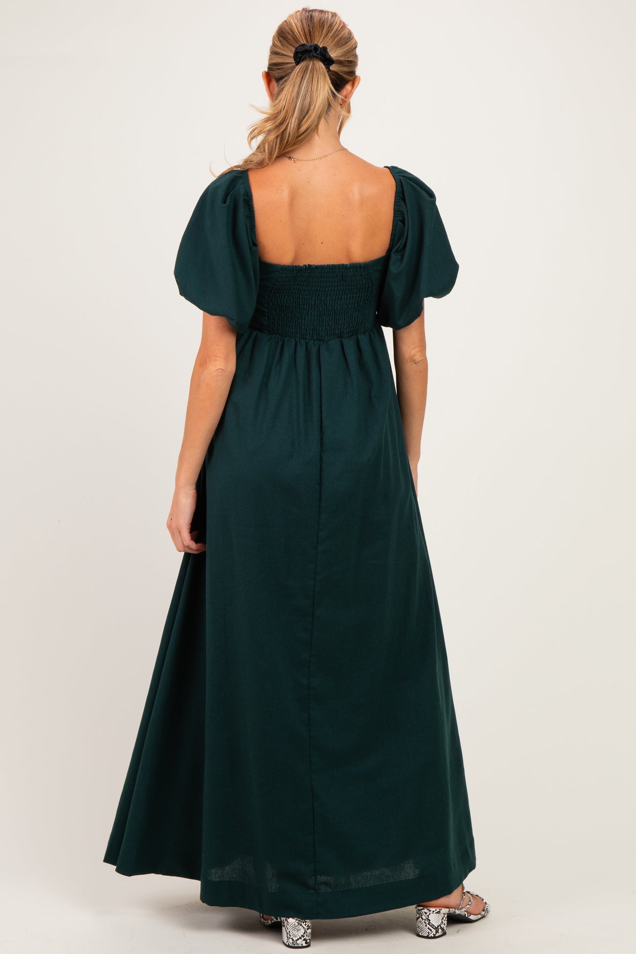 woman wearing a dark green maternity maxi dress with puff sleeves and a smocked back, showing her baby bump