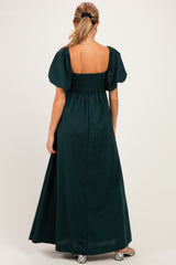 woman wearing a dark green maternity maxi dress with puff sleeves and a smocked back, showing her baby bump