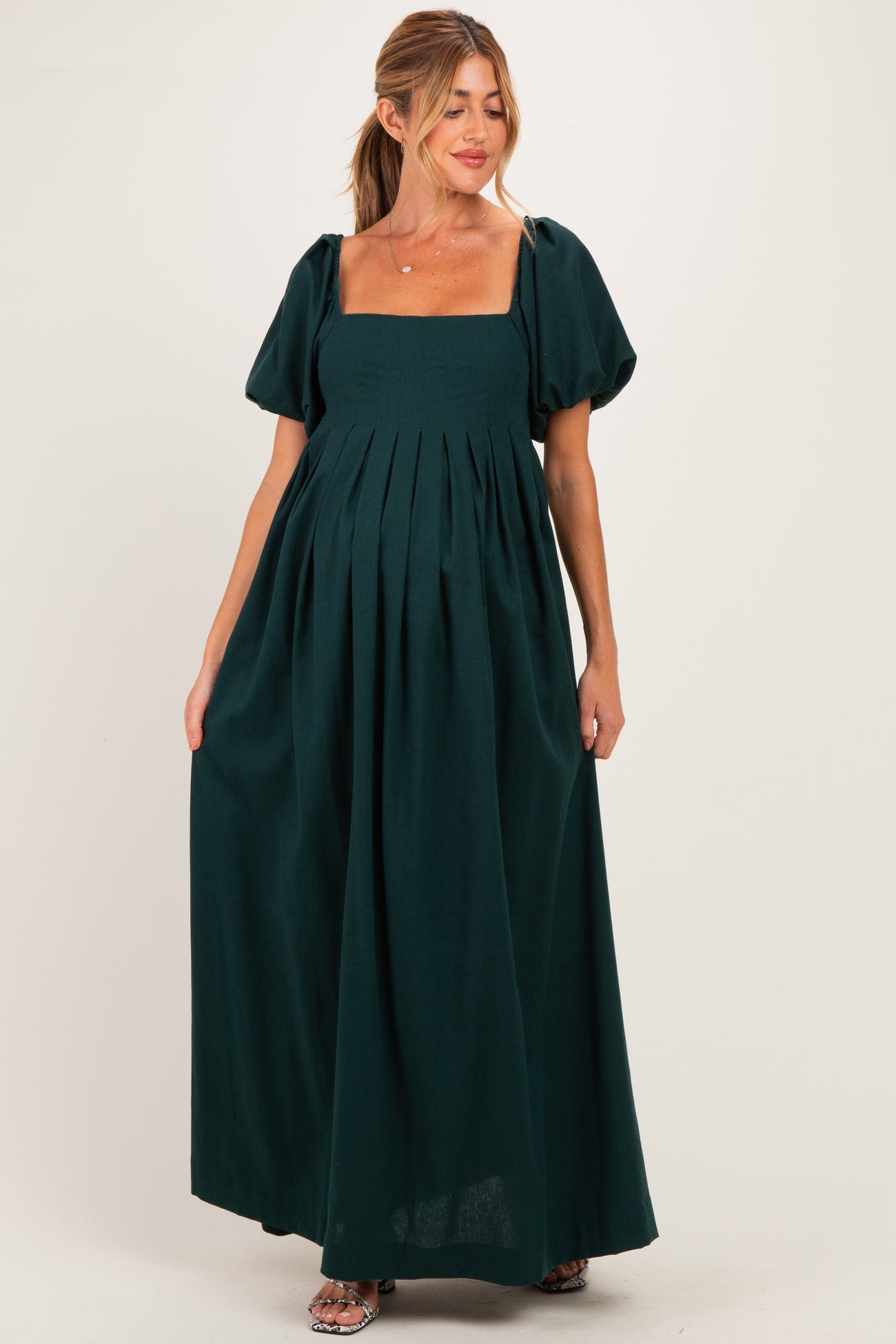 woman wearing a dark green maternity maxi dress with puff sleeves and a square neckline, showing baby bump