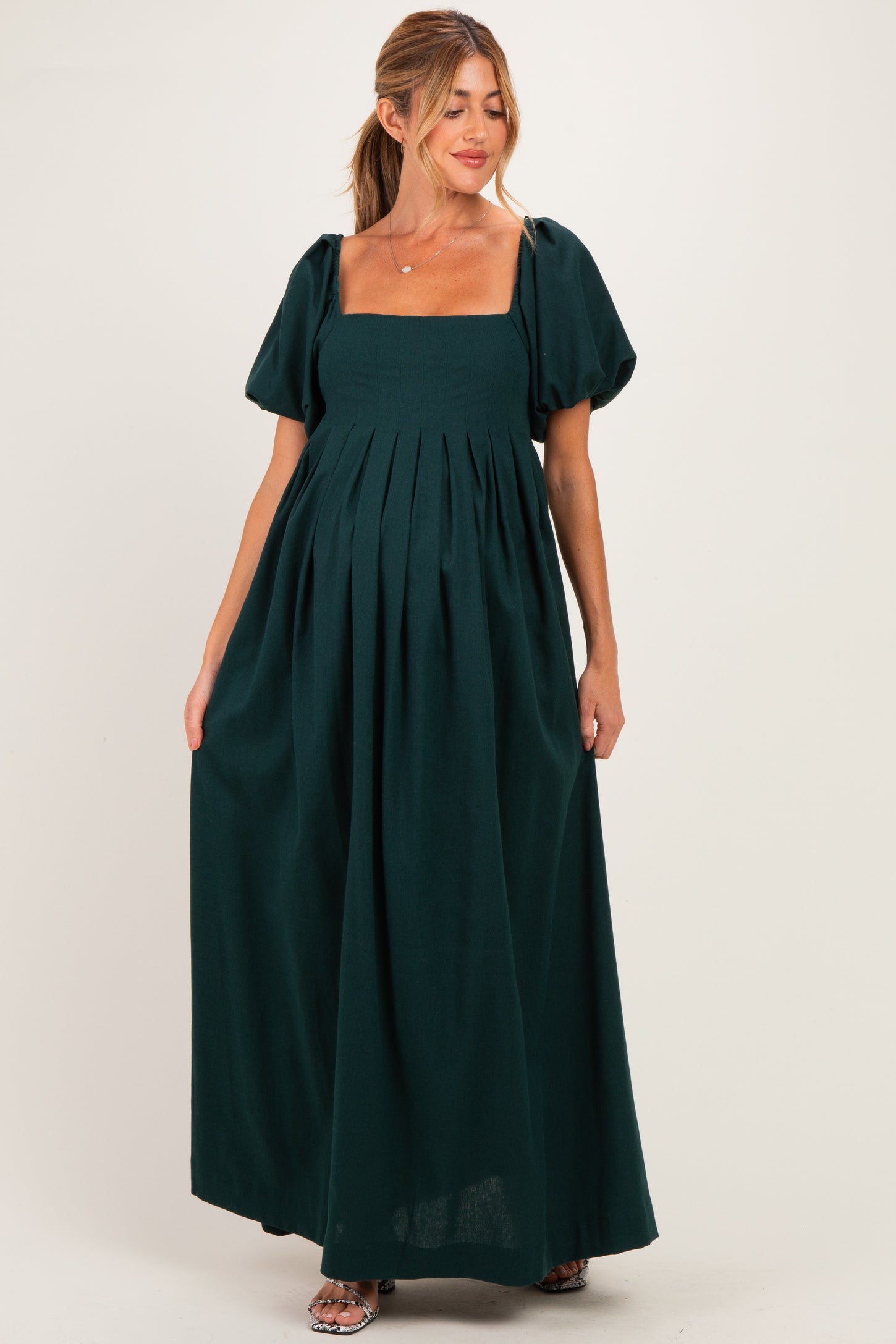 woman wearing a dark green maternity maxi dress with puff sleeves and a square neckline, showing baby bump