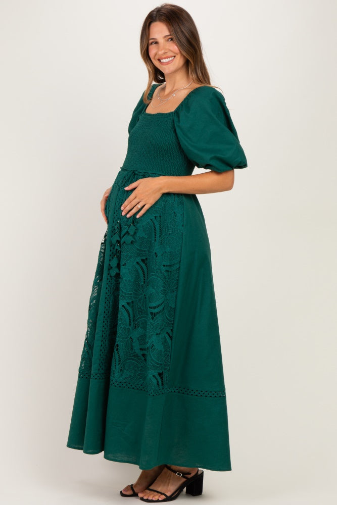 woman wearing a dark green maternity dress with puff sleeves and embroidered lace detailing, showing her baby bump