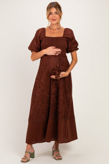woman wearing a brown maternity dress with puff sleeves and embroidery, holding her baby bump