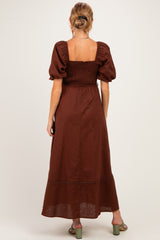 woman wearing a brown maternity maxi dress with puff sleeves and smocked bodice, showing the back view