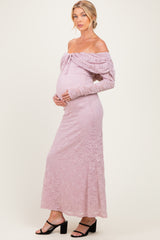 woman wearing a light pink off-the-shoulder lace maternity dress, gently cradling her baby bump