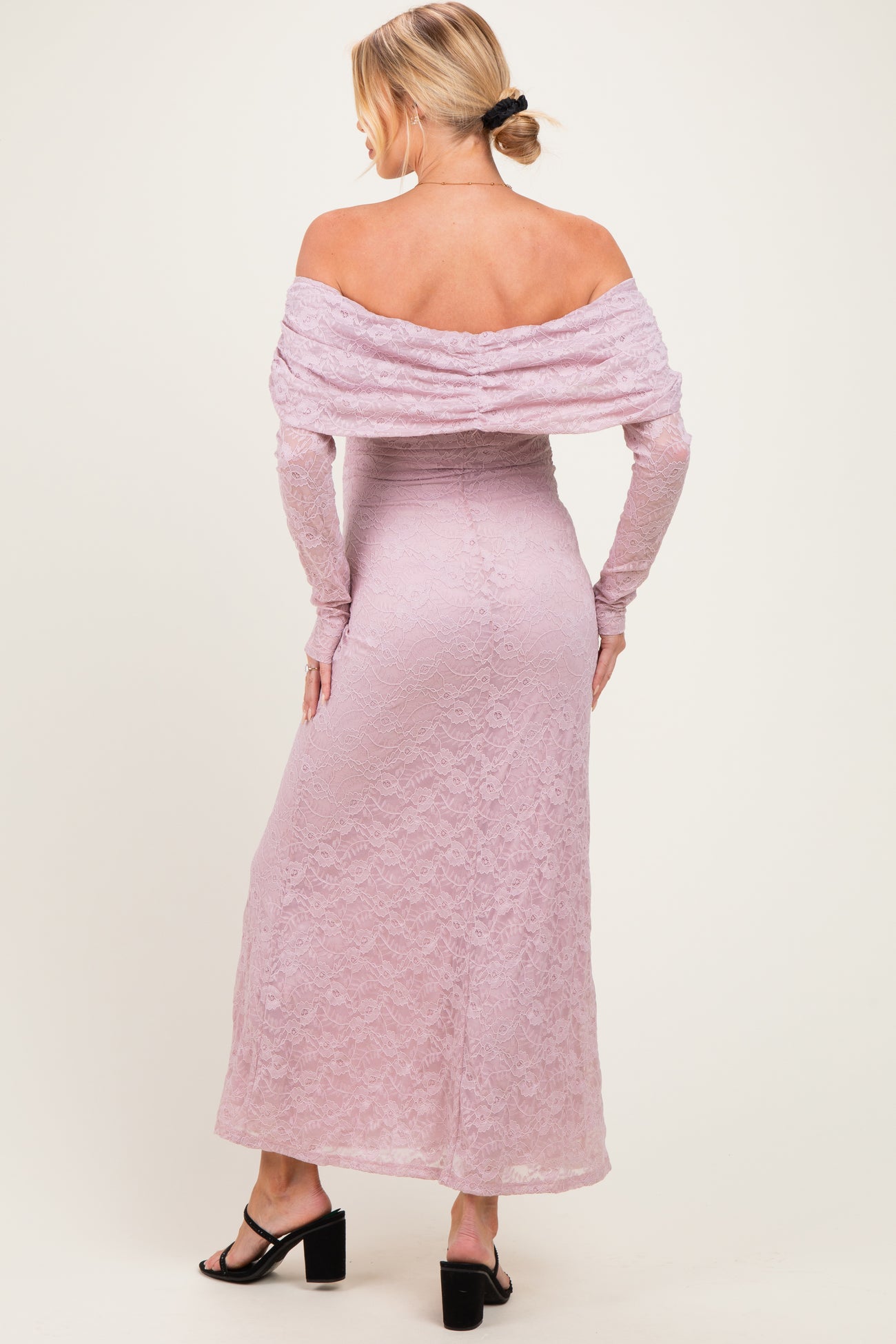 woman wearing a blush pink off-shoulder lace maternity dress with long sleeves and a fitted silhouette