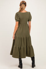 woman wearing a dark green maternity midi dress with puff sleeves and a tiered skirt, showing her baby bump