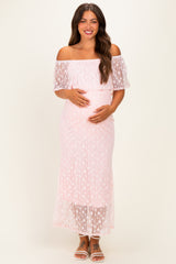 woman wearing a light pink off-the-shoulder lace maternity dress and holding her baby bump