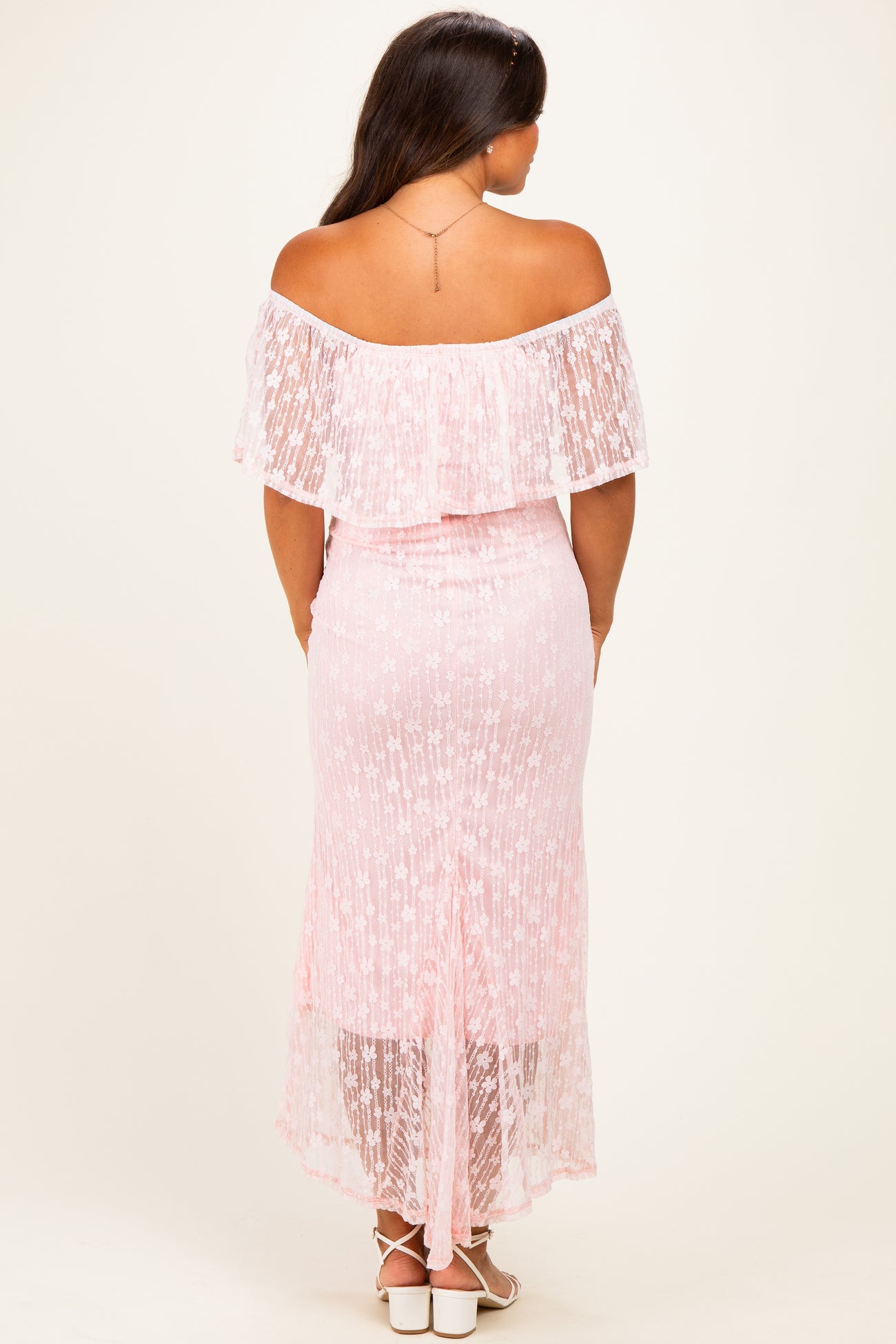 woman wearing a pink off-the-shoulder maternity dress with lace details and a high-low hem, showing a baby bump