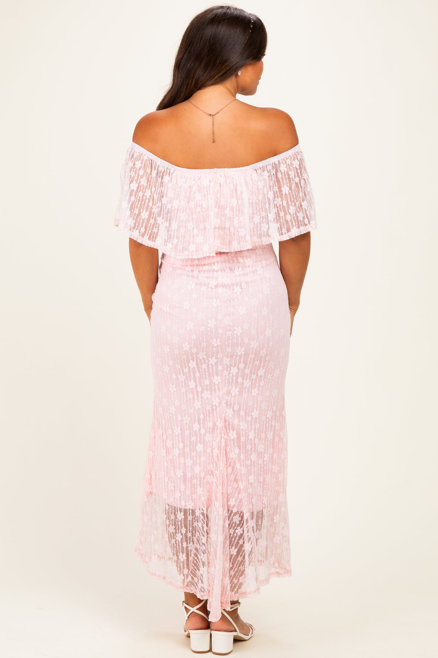 woman wearing a pink off-the-shoulder maternity dress with lace details and a high-low hem, showing a baby bump