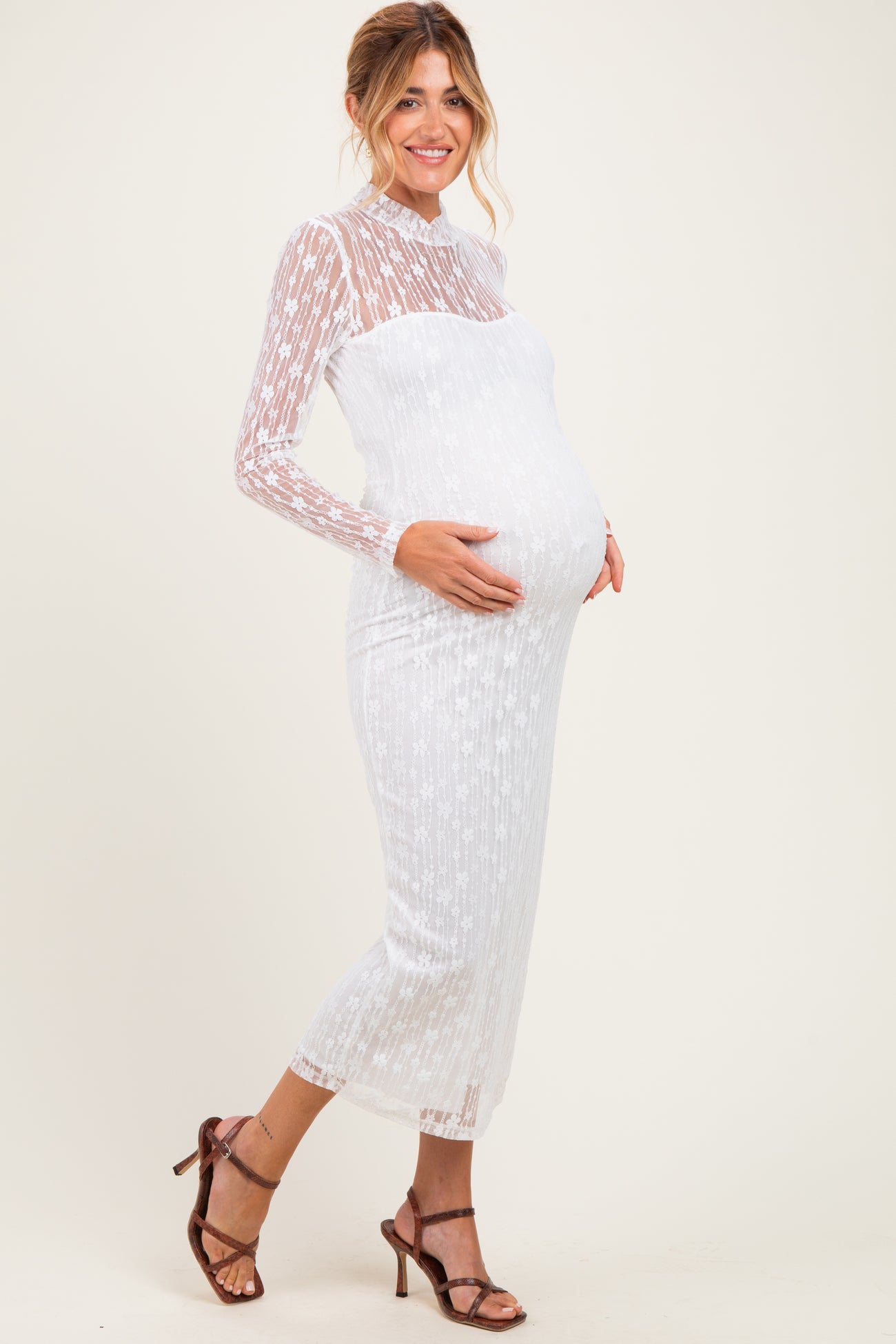 woman wearing a sheer white long sleeve maternity dress highlighting her baby bump paired with strappy heels