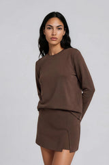 woman wearing a brown long sleeve sweatshirt and a matching mini skirt with a side slit