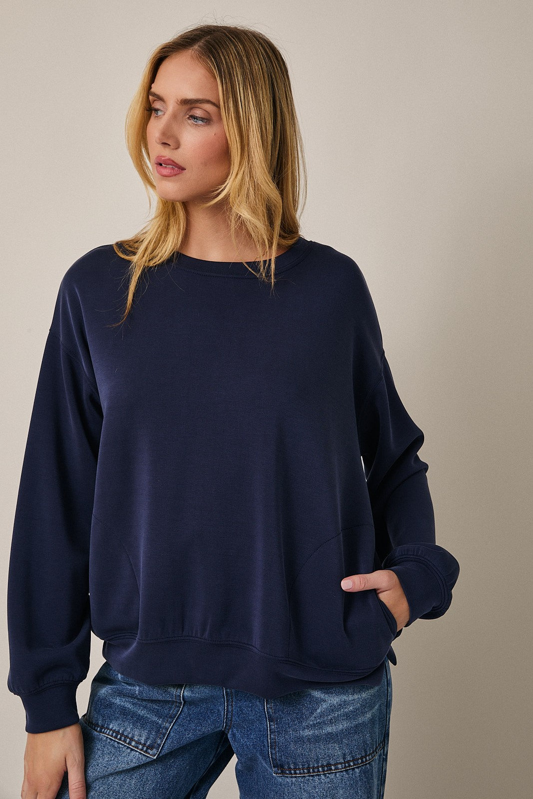 woman wearing a navy oversized sweatshirt with a round neckline and a front pocket, styled with casual jeans