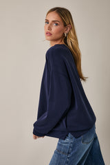 woman wearing a navy blue oversized sweatshirt and blue jeans, posing with her head turned to the side