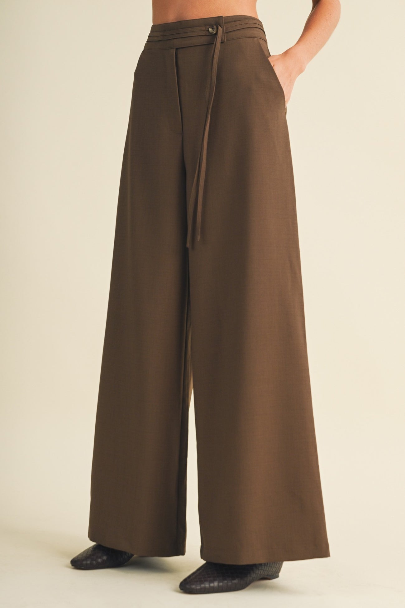 woman wearing brown wide-leg trousers with a tied waist and side pockets