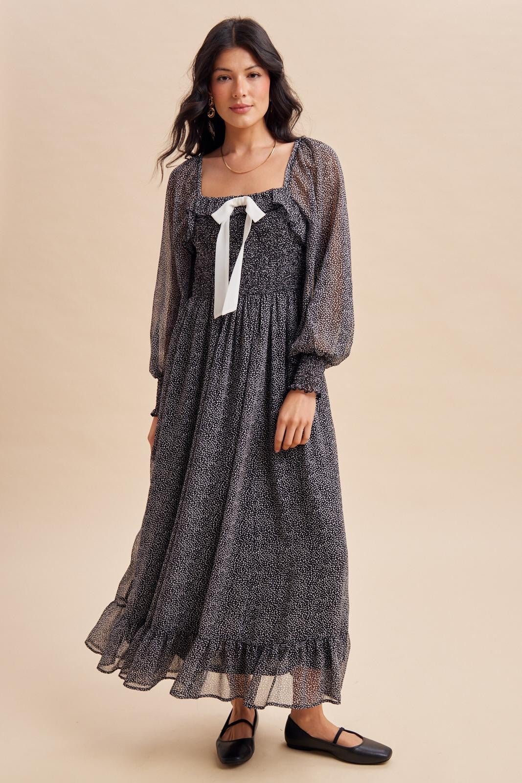 woman wearing a black and white polka dot maxi dress with puff sleeves and a ribbon tie at the neck
