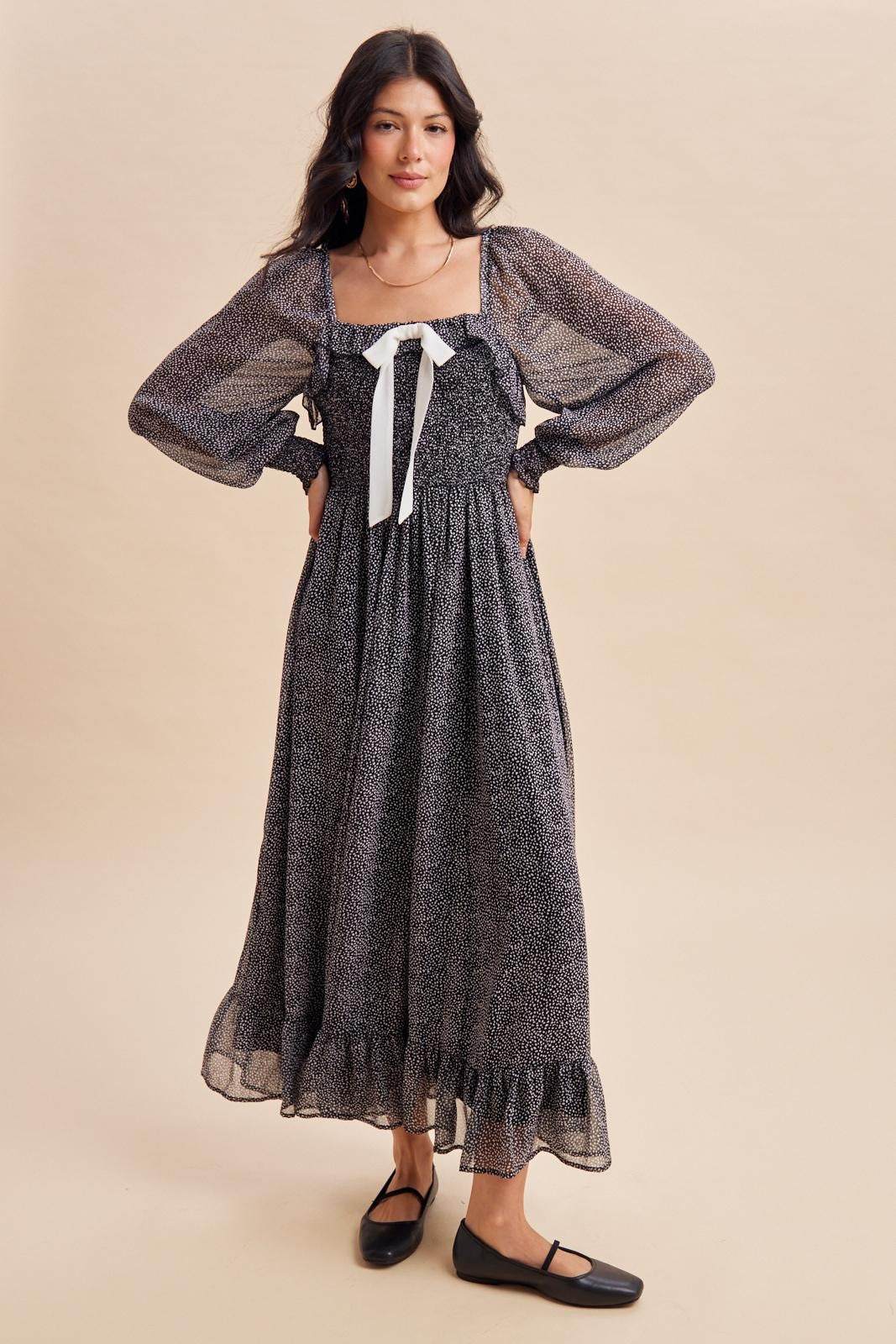 woman wearing a black and white floral maxi dress with long puff sleeves and a front bow detail